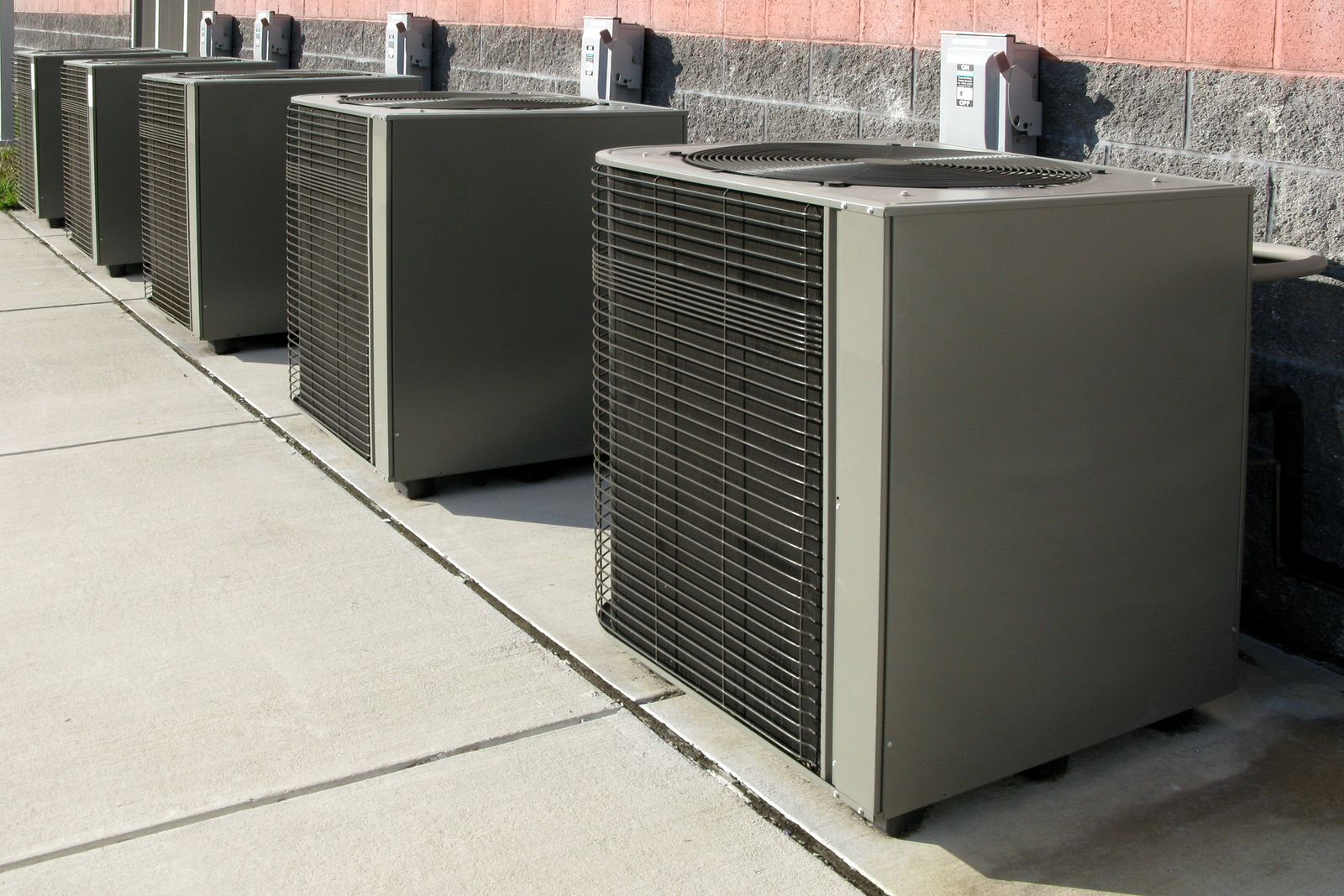 Row of commercial HVAC air conditioner compressor units outside a commercial building as elements of a climate control cooling and refrigeration conditioning system