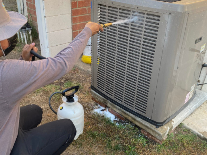 Technician cleaning outdoor heat pump unit during maintenance service